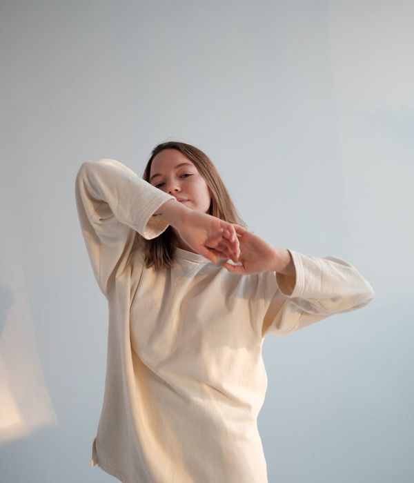 Woman in a comfortable outfit performing a gentle stretching movement in a minimalist room.